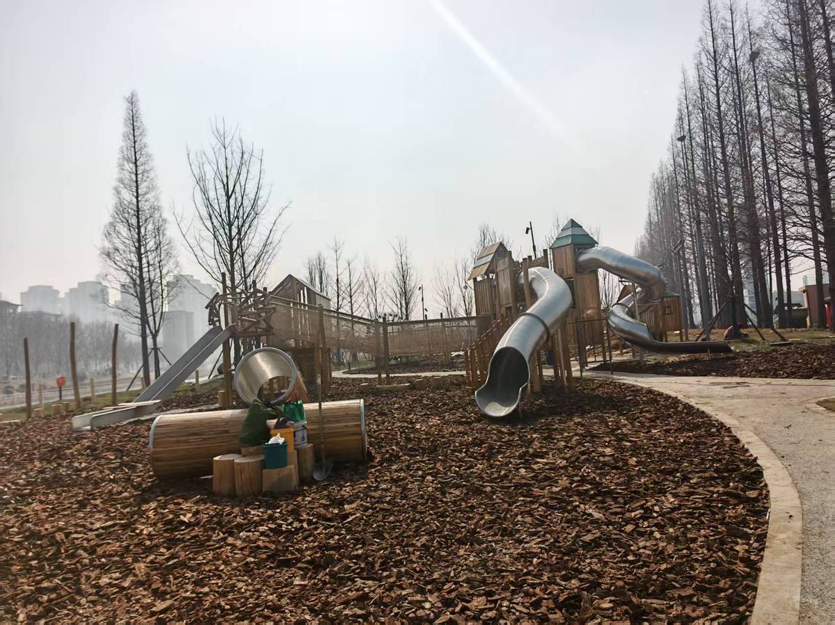 rope tube slide and open timber platforms inside a low age play zone with wood chip surfacing Tobogán de tubo de cuerda y plataformas de madera abiertas dentro de una zona de juegos de baja edad con superficie de astillas de madera