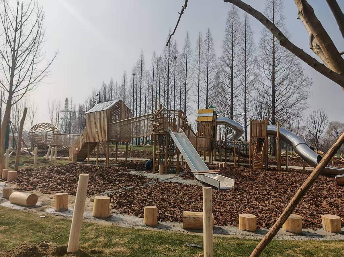 low timber play tower with stainless steel slides set inside a wood chip surfacing area for children under six Torre de juegos baja de madera con toboganes de acero inoxidable ubicada dentro de un área de superficie con astillas de madera para niños menores de seis años